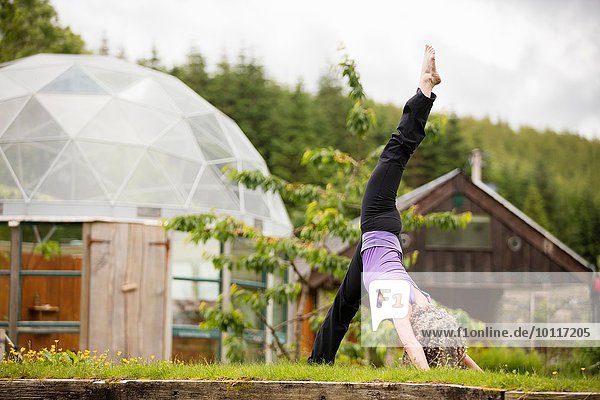 Reife Frau  die Yoga praktiziert  mit einem Bein im Garten der Öko-Lodge.