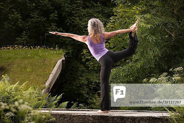 Reife Frau,  die Yogatänzerin ist,  posiert im Garten.