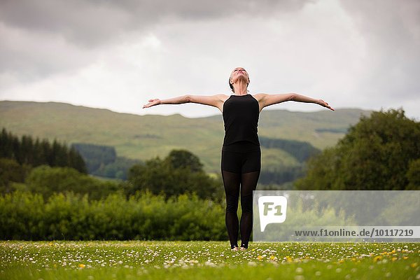 Reife Frau übt Yogastellung mit offenen Armen im Feld