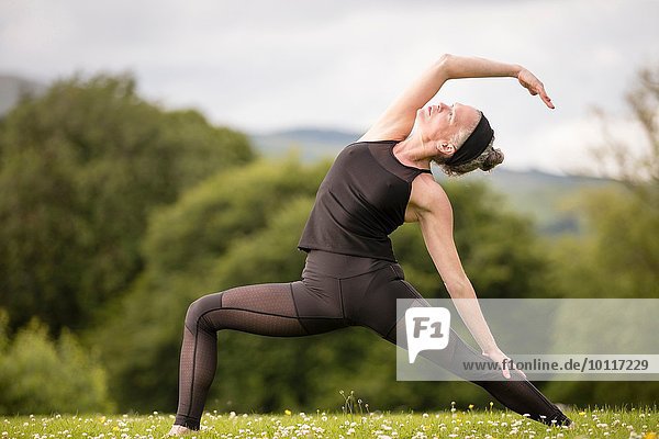 Reife Frau praktiziert Yoga-Pose im Feld