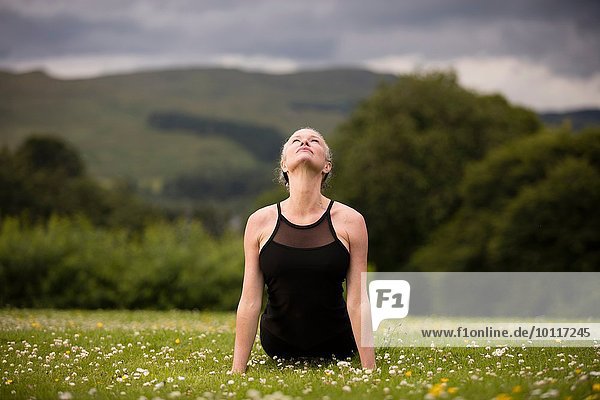 Reife Frau praktiziert Yogakobra-Position im Feld