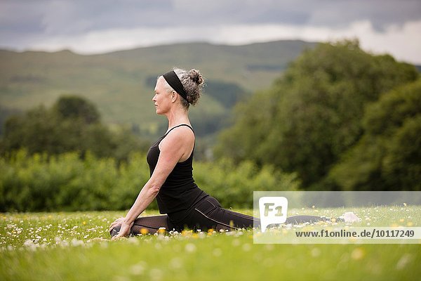 Mature woman doing splits practicing yoga position in field