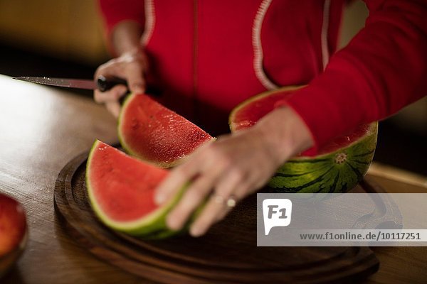 Ausschnitt einer reifen Frau beim Schneiden von Wassermelone in der Küche