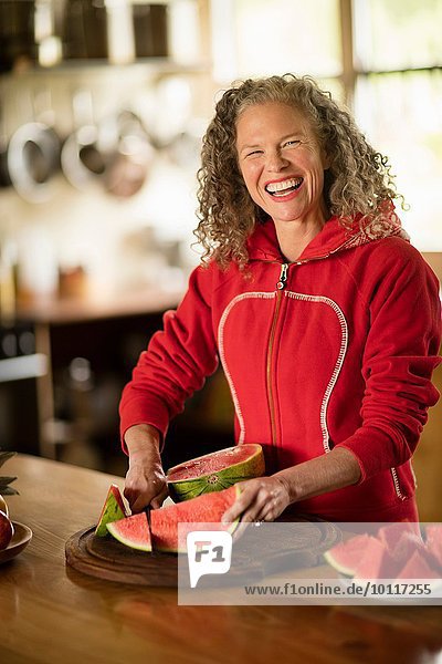 Porträt einer reifen Frau beim Schneiden von Wassermelone in der Küche