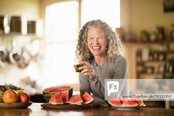 Porträt einer reifen Frau beim Essen von Wassermelone in der Küche