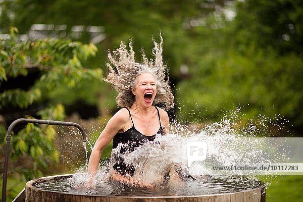 Reife Frau  die beim Öko-Retreat in ein frisches Kaltwasserbecken spritzt.