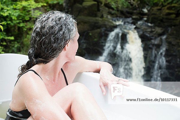Reife Frau im Schaumbad mit Blick auf den Wasserfall beim Öko-Retreat