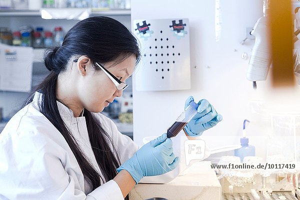 Wissenschaftlerin betrachtet Probenflasche im Labor