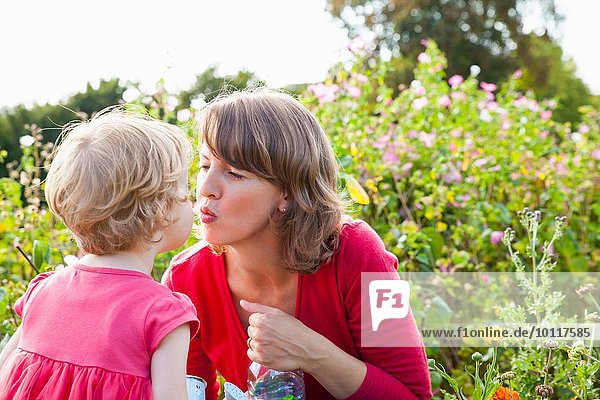 Mittlere erwachsene Mutter und Kleinkind Tochter beim Küssen im Blumenfeld