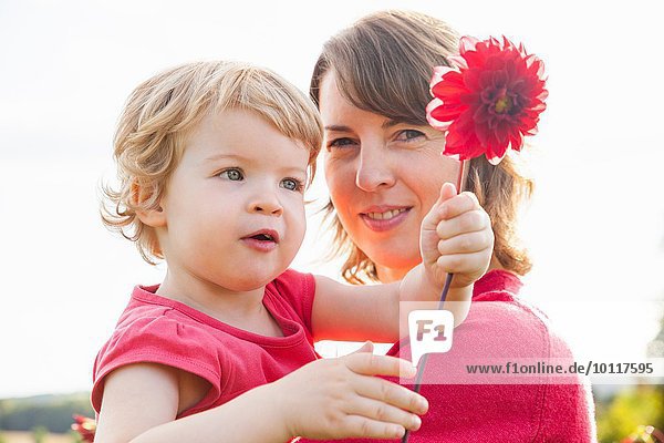 Porträt der mittleren erwachsenen Mutter und Kleinkindstochter mit roter Blume im Feld