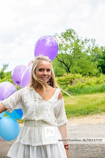 Portrait of pretty young woman with bunch of balloons on rural road