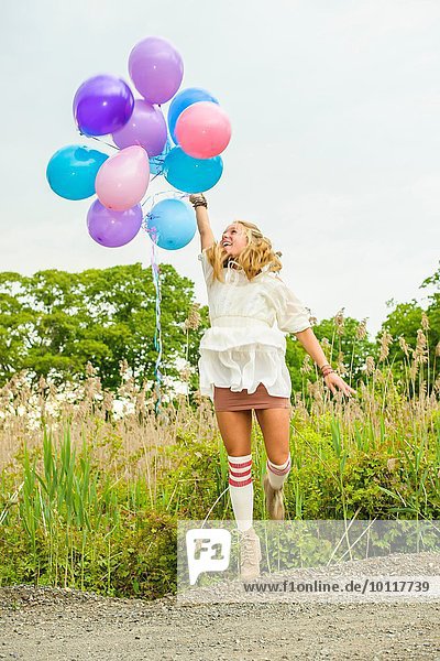 Junge Frau springt mit Luftballons auf der Landstraße