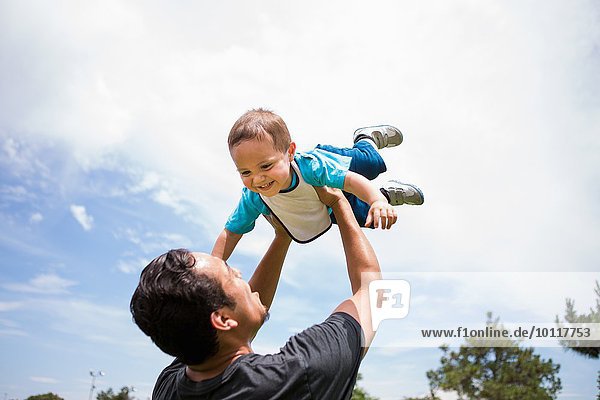 Young man playing lifting up toddler brother in park