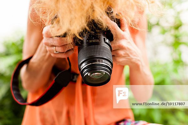Abgeschnittene Aufnahme einer Frau mit roten Haaren  die mit der digitalen Spiegelreflexkamera nach unten fotografiert.