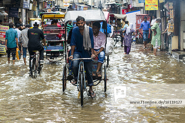 Menschen gehen und Fahrrad-Rikschas fahren durch die nach einem heftigen Monsunregenfall überfluteten Straßen der Vorstadt Paharganj  Neu-Delhi  Delhi  Indien  Asien