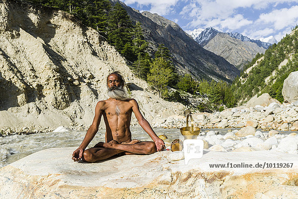 Mahant Naomi Giri  52 Jahre  Sadhu  im Lotussitz  padmasana  auf einem Felsen am Ufer des heiligen Flusses Ganges  bei der Meditation  Gangotri  Uttarakhand  Indien  Asien