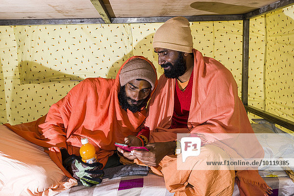 Zwei Sadhus  heilige Männer  spielen in einem Zelt auf einem Smartphone  Kedarnath  Uttarakhand  Indien  Asien