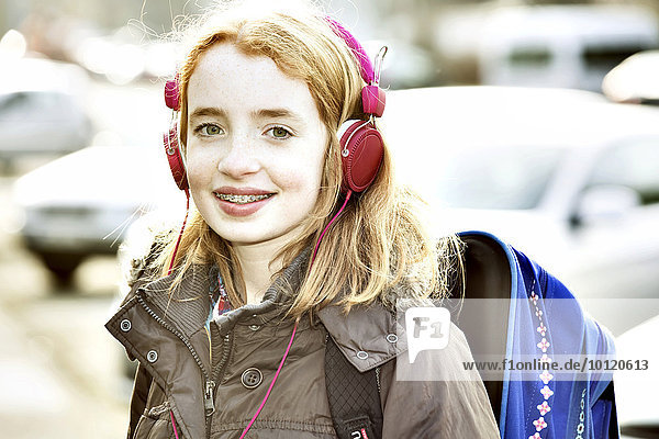 Mädchen mit Schulranzen und Kopfhörern auf dem Schulweg