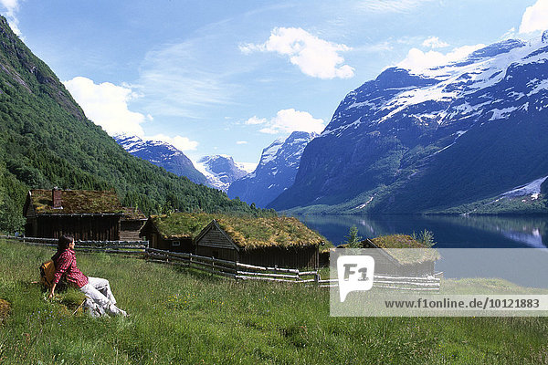 Woman sitting in front of old houses on the shores of Lovatnet  Lake Loen  near the Nordfjord  Norway  Scandinavia  Europe