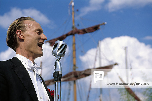Man singing into a vintage microphone during the Kieler Woche or Kiel Week sailing regatta  Kiel  Schleswig-Holstein  Germany  Europe