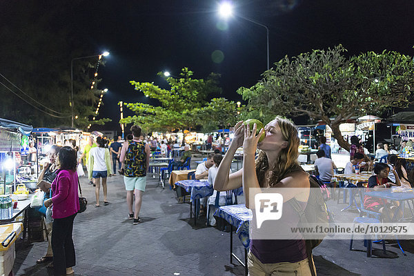 Frau  Touristin trinkt auf einem Nachtmarkt eine Kokosnuss  Na Thon  Insel Koh Samui  Thailand  Asien
