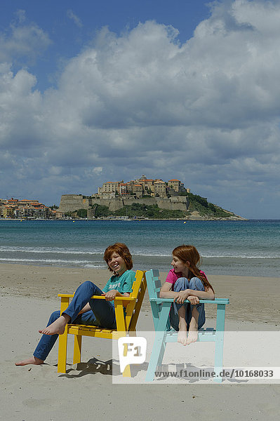 Kinder sitzen in bunten Strandstühlen am Strand von Calvi  Département Haute-Corse  Korsika  Frankreich  Europa