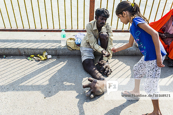 A beggar with Elephantiasis at his feet is receiving some money from a girl at Harki Pauri Ghat at the holy river Ganges  Haridwar  Uttarakhand  India  Asia