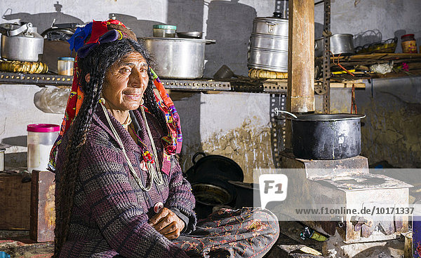 Frau des Brokpa-Stammes  bei der Küchenarbeit  in traditioneller Kleidung mit typischem Blumen-Kopfschmuck  Dah Hanu  Jammu und Kaschmir  Indien  Asien