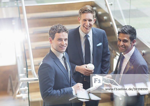 Portrait confident businessmen with coffee and digital tablet on stairs