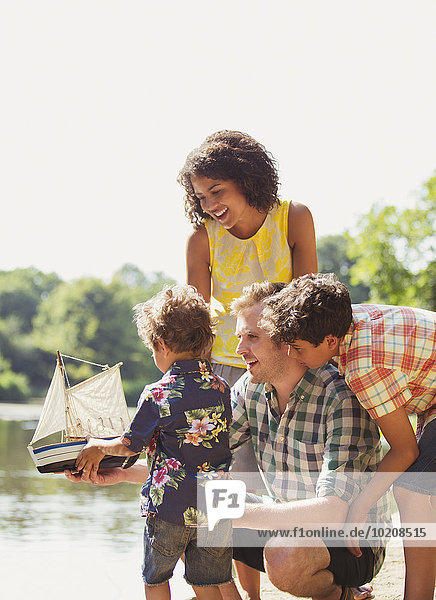 Familie mit Spielzeug-Segelboot am sonnigen Seeufer