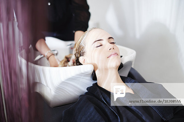 Customer with eyes closed getting hair washed in salon