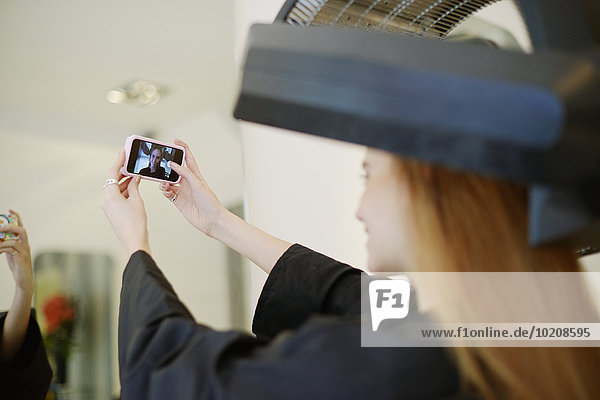 Customer taking selfie with camera phone in hair salon