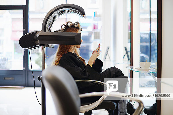 Woman sitting under dryer texting with cell phone in hair salon