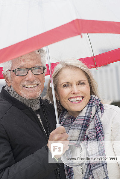 Older Caucasian couple standing under umbrella