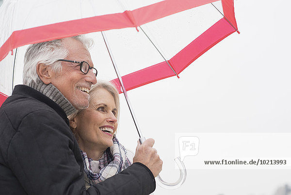 Older Caucasian couple standing under umbrella