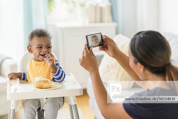 Mixed race mother photographing messy baby boy in high chair