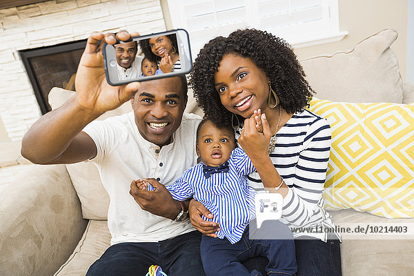 Black family taking selfie on sofa in living room