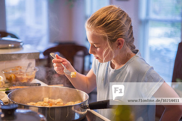 Caucasian girl tasting food and cooking in kitchen
