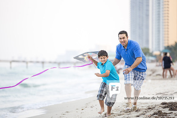 Hispanic father and son flying kite on beach