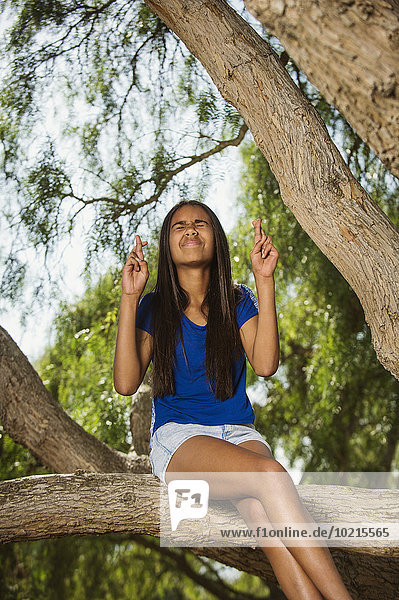 Mixed race girl crossing fingers on tree branch