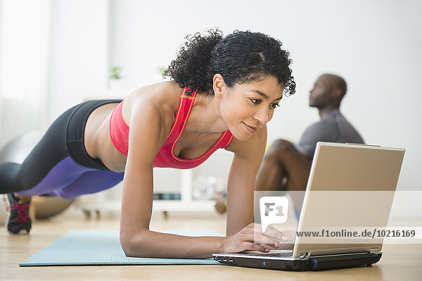 Woman using computer and doing push-ups in gym