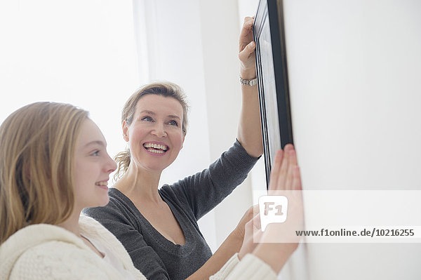 Caucasian mother and daughter hanging picture on wall