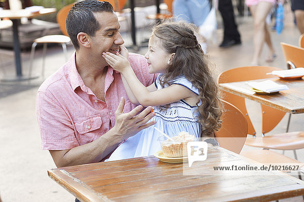 Hispanic father and daughter eating at sidewalk cafe