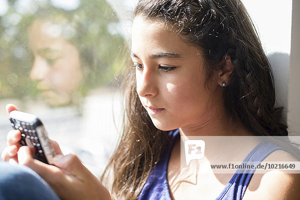 Mixed race girl using cell phone at window
