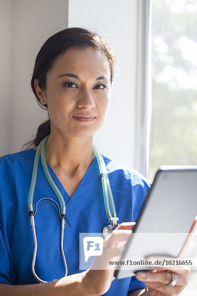 Mixed race nurse using digital tablet at window