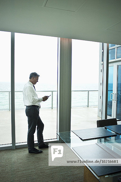 Caucasian businessman using cell phone at office window