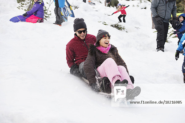 Hispanic couple sledding on snowy hillside