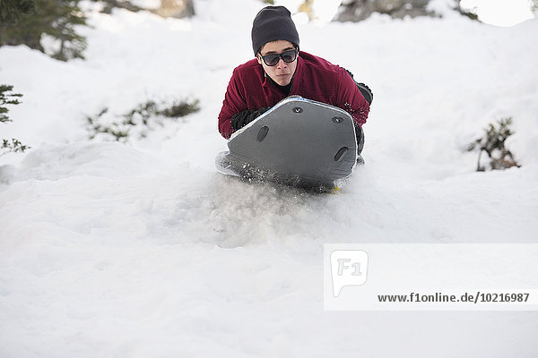 Hispanic man sledding on snowy hillside