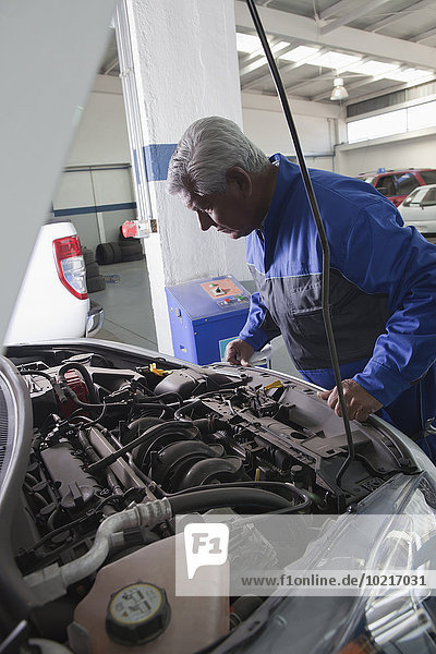 Older Hispanic mechanic examining car in garage