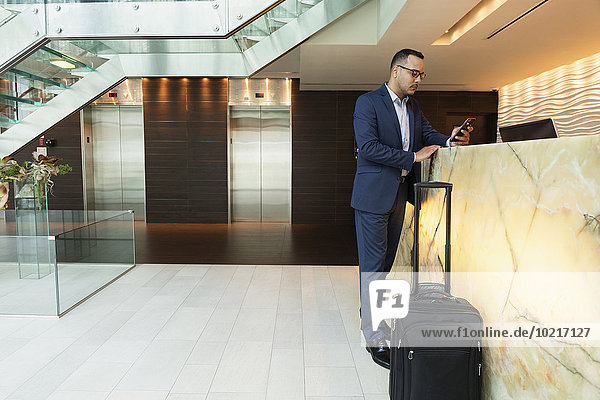 Hispanic businessman using cell phone at hotel front desk